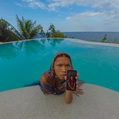 A woman leaning onto the edge of a swimming pool, holding a mobile phone 